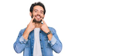 Gündelik kıyafetler giymiş, ağzı açık gülümseyen, parmakları işaret eden ve neşeli gülümsemeye zorlayan genç İspanyol bir adam. 