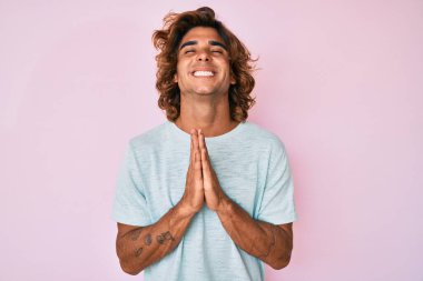 Gündelik giysiler giyen genç İspanyol adam elleri bağlı yalvarıyor ve dua ediyor. Yüzünde umut ifadesi var. Çok duygusal ve endişeli. Yalvarıyor. 