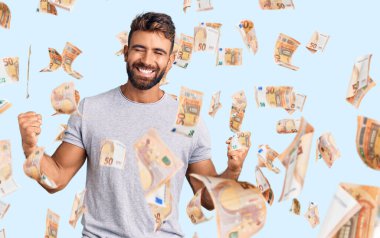 Gündelik kıyafetler giyen genç İspanyol adam çok mutlu ve heyecanlı. Kazanan jestler yapıyor. Kolları havada, gülümsüyor ve başarı için bağırıyor. kutlama konsepti.