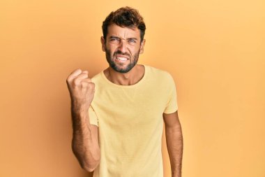 Sarı arka plan üzerine sarı tişört giyen yakışıklı bir adam öfkeyle bağırırken sinirli ve öfkeli bir şekilde yumruğunu kaldırıyor. öfke ve agresif konsept. 