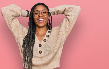 Afro-Amerikalı kadın günlük kıyafetler giyiyor rahatlıyor ve esniyor, kolları ve elleri başının arkasında mutlu bir şekilde gülümsüyor. 