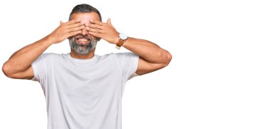 Orta yaşlı yakışıklı bir adam, günlük beyaz tişörtler giyip gözleri kapayarak neşeli ve komik gülümsüyor. kör kavram. 