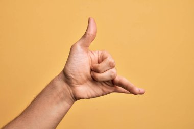 Kafkas genci parmaklarını izole edilmiş sarı arka planda gösteriyor Hawaii Shaka selamlama hareketi, telefon ve iletişim sembolü.