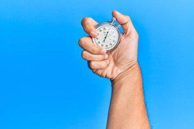 İzole edilmiş mavi arka plan üzerinde kronometre kullanan İspanyol bir adamın eli..
