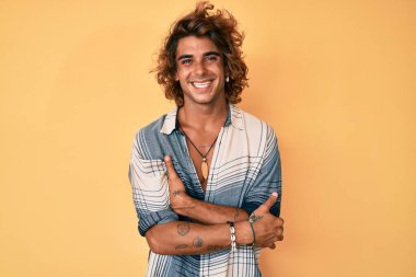 Yaz stili gülen yüz takınan genç İspanyol adam kollarını kavuşturup kameraya bakıyor. pozitif kişi. 