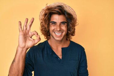 Yazlık şapkalı genç İspanyol adam olumlu gülümsüyor ve el ve parmaklarıyla imza atıyor. başarılı ifade. 