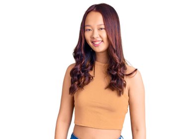 Genç, güzel Çinli kız günlük kıyafetler giyiyor. Pozitif ve mutlu görünüyor. Kendine güvenen bir gülümsemeyle dişlerini gösteriyor. 