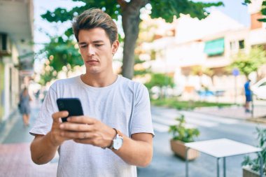 Şehirde akıllı telefon kullanan, ciddi bir suratı olan beyaz bir genç..