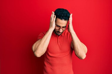 Günlük kıyafetler ve gözlük takan genç İspanyol adam baş ağrısı ve stres yüzünden acı çekiyor çünkü acı ve migren. Eller başının üstünde.. 