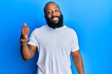 Sıradan beyaz tişört giyen, gülümseyen, gülümseyen ve baş parmağıyla yüzünü gösteren Afro-Amerikan genç adam.. 