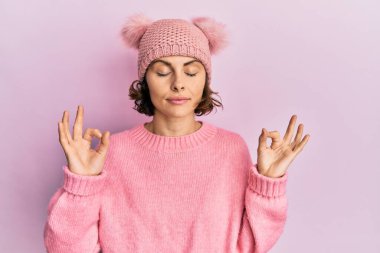 Şirin yün şapkalı esmer kadın rahatla ve gözleri kapalı gülümse parmaklarıyla meditasyon hareketi yapıyor. yoga konsepti. 