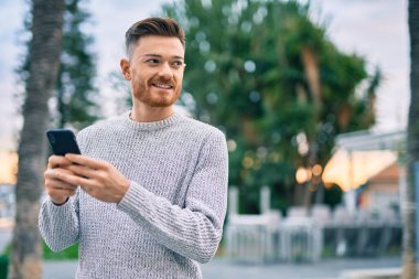 Beyaz adam şehirde akıllı telefon kullanarak mutlu bir şekilde gülümsüyor..