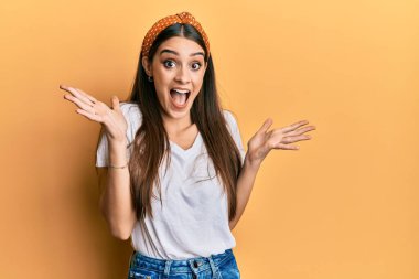 Güzel esmer, beyaz tişört giyen genç bir kadın çılgınlığı kutluyor ve başarıyı kolları açık ve gözleri açık heyecanla haykırarak kutluyor. Kazanan konsept 