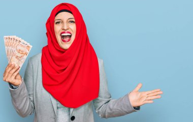 İslami tesettür takan güzel İspanyol kadın elinde Türk lirası banknotlarla zaferi kutluyor mutlu bir gülümsemeyle ve ellerini kaldırarak kazanan ifadeyle. 