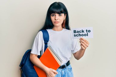 Sırt çantası takan genç İspanyol kız okul afişini geri çekiyor. Hiçbir şeyden haberi yok ve kafası karışık. şüphe kavramı. 