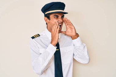 Uçak pilotu üniforması giyen genç İspanyol adam elleri ağızda bağırarak bağırıyor. 