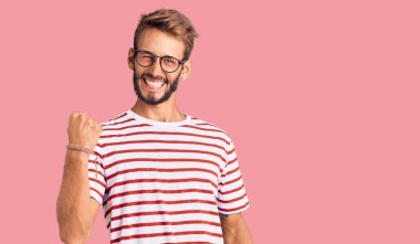 Sıradan kıyafetler ve gözlük takan sakallı yakışıklı sarışın adam kolları havada ve gözleri kapalı bir şekilde başarıyı kutluyor ve şaşırıyor. Kazanan konsept. 