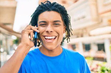 Genç Afrikalı Amerikalı gülümseyen mutlu bir adam şehrin caddesinde akıllı telefondan konuşuyor..