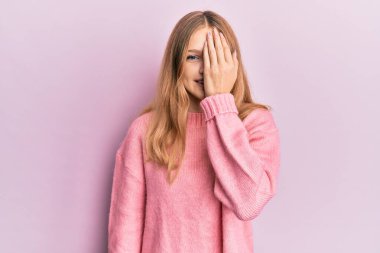 Güzel, genç, beyaz bir kız günlük kıyafetler giyiyor. Bir gözünü eliyle kapatıyor. Yüzünde kendine güvenen bir gülümseme ve sürpriz bir duygu var.. 