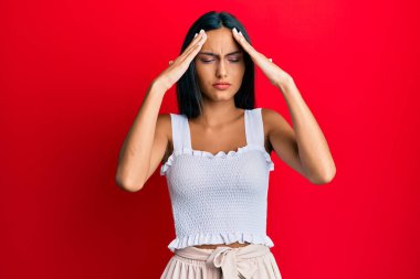 Genç esmer kadın, elleri kafasında günlük kıyafetler giyiyor, stres yüzünden baş ağrısı çekiyor. migren ağrısı. 