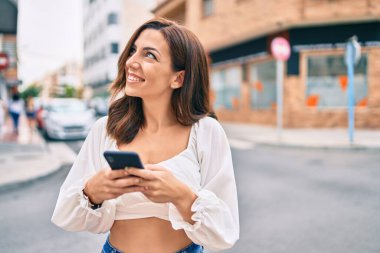 Genç İspanyol kadın şehirde akıllı telefon kullanarak mutlu bir şekilde gülümsüyor..