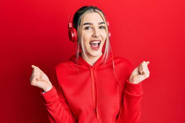 Spor kıyafetleri giyen ve kulaklık takan genç çağdaş bir kız, başarı için şaşırmış ve şaşırmış bir şekilde kollarını kaldırıp gözleri açık bir şekilde kulaklık takıyor. Kazanan konsept. 