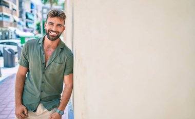 Genç İspanyol adam gülümsüyor. Mutlu bir şekilde şehrin duvarına yaslanıyor.