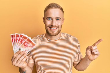 Kafkasyalı genç adam elinde 20 İsrail şekeri banknotları tutarken mutlu bir şekilde gülümsüyor. 