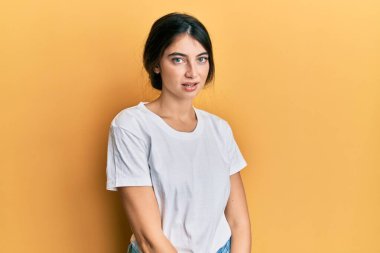 Yüzünde ciddi bir ifade olan günlük beyaz tişört giyen genç beyaz bir kadın. Basit ve doğal bir şekilde kameraya bakıyorsun.. 