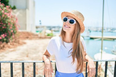 Genç sarışın kadın tatilde mutlu bir şekilde gülümsüyor. Kentin caddesinde korkuluklara yaslanıyor.