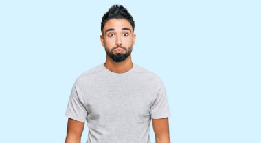 Sakallı, sıradan gri tişörtlü, komik suratlı, yanakları şişen genç bir adam. Havayla şişmiş ağız, çılgın bir ifade.. 