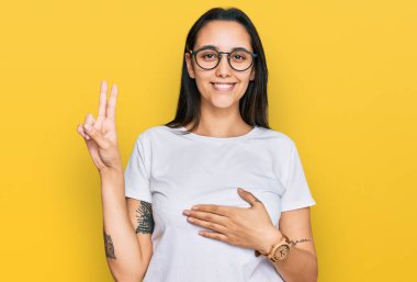 Young hispanic woman wearing casual white t shirt smiling swearing with hand on chest and fingers up, making a loyalty promise oath 