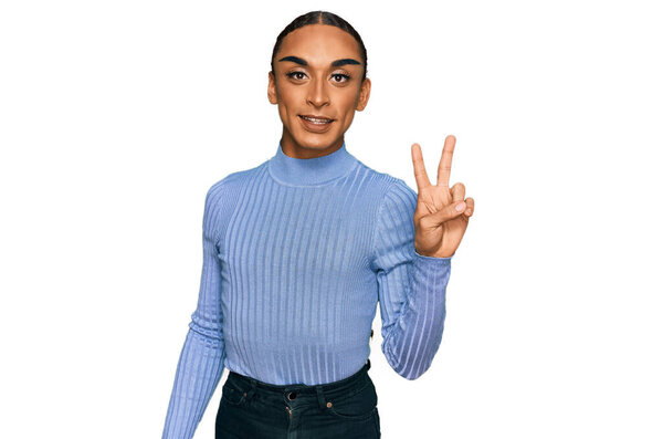 Hispanic transgender man wearing make up and long hair wearing casual clothes smiling with happy face winking at the camera doing victory sign. number two. 