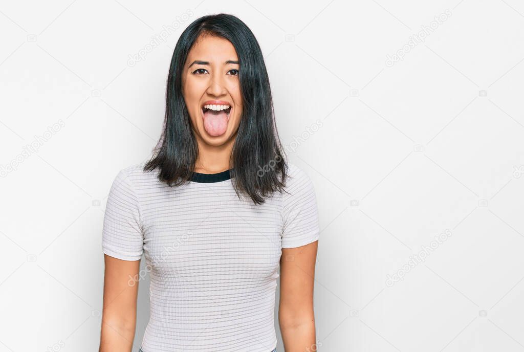 Beautiful asian young woman wearing casual white t shirt sticking tongue out happy with funny expression. emotion concept. 