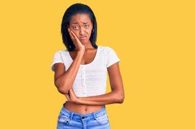 Genç Afro-Amerikalı kadın günlük kıyafetler giyip kollarını kavuşturarak depresyondan sıkılmış ve yorgun görünüyor.. 