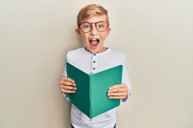 Küçük beyaz çocuk kitap okuyor. Gözlük takıyor. Çılgınca kutlama yapıyor.. 