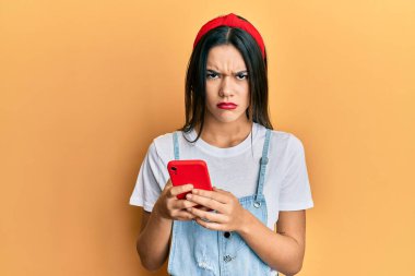 Genç İspanyol kız akıllı telefon kullanıyor şüpheci ve gergin, sorun yüzünden surat asıyor. negatif kişi. 