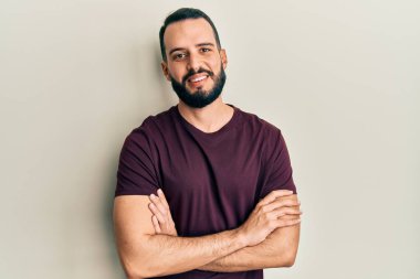 Sıradan tişörtler giyen sakallı genç adam kollarını kavuşturup kameraya bakarken gülümsüyor. pozitif kişi. 