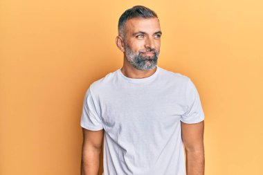 Orta yaşlı beyaz tişört giyen yakışıklı bir adam gülümsüyor, yan tarafa bakıyor ve düşünüyor.. 