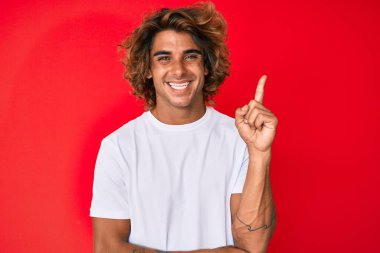 Gündelik beyaz tişört giyen genç İspanyol adam gülümsüyor mutlu bir şekilde elini ve parmağını yana doğru gösteriyor. 