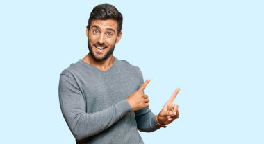 Yakışıklı, sıradan kıyafetler giyen, gülümseyen ve kameraya bakan, iki elini ve parmağını yana doğru gösteren İspanyol bir adam.. 