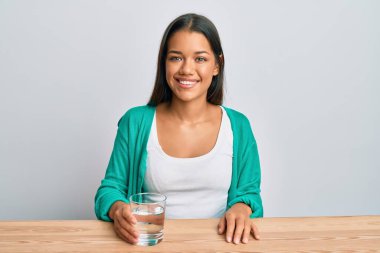 Güzel İspanyol kadın bir bardak su içiyor. Pozitif ve mutlu görünüyor. Duruyor ve gülümsüyor. 