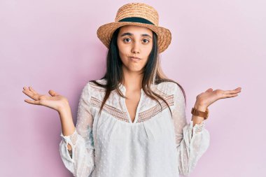 Yaz şapkası takan genç İspanyol kadın habersiz ve kolları açık, hiçbir fikri yok ve şüpheli bir yüzü var.. 