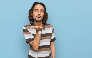 Gündelik giysiler giymiş genç İspanyol bir adam kameraya bakıp havada bir öpücük savuruyor ve sevimli ve seksi oluyor. aşk ifadesi. 