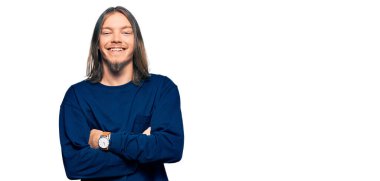 Uzun saçlı, kışlık süveter giyen, kollarını kavuşturup kameraya gülümseyen yakışıklı beyaz adam. pozitif kişi. 