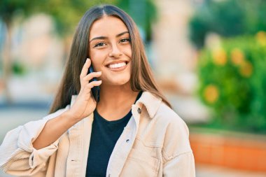 Genç İspanyol kız gülümsüyor. Parktaki akıllı telefondan konuşarak mutlu oluyor..