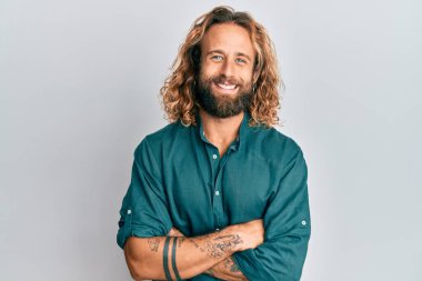 Sakallı, uzun saçlı, sıradan kıyafetler giyen kolları çapraz gülümseyen ve kameraya bakan yakışıklı bir adam. pozitif kişi. 