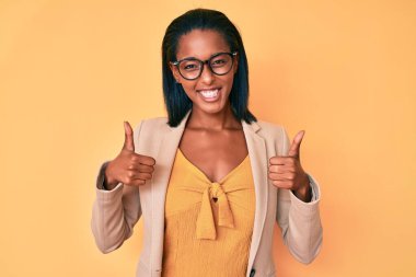 Genç afro-amerikan kadın iş kıyafetleri giyiyor başarı işareti yapıyor, elleriyle olumlu jest yapıyor, gülümsüyor ve mutlu. Neşeli ifade ve kazanan jest. 