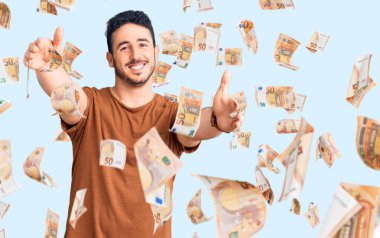 Gündelik giysiler giymiş genç İspanyol adam kameraya bakıp sarılmak için kollarını açmış gülümsüyor. Mutluluğu kucaklayan neşeli bir ifade..