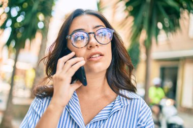 Endişeli yüzüyle şehirde akıllı telefondan konuşan genç İspanyol iş kadını..